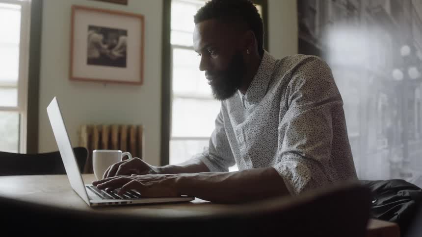 A man types on a laptop while sitting at a table