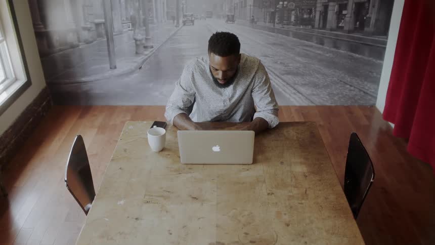 A man working on a laptop at a table with a cup and phone