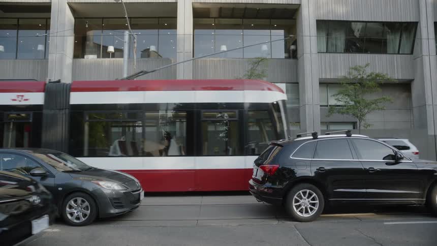 Cars and a passenger train travel on a city street