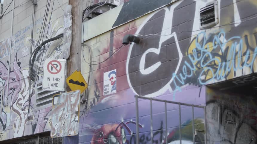 The camera focuses on the graffiti covered wall of a building