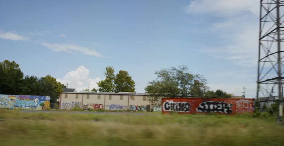 Driving by abandoned rail cars and buildings with graffiti art on the side of a railroad track