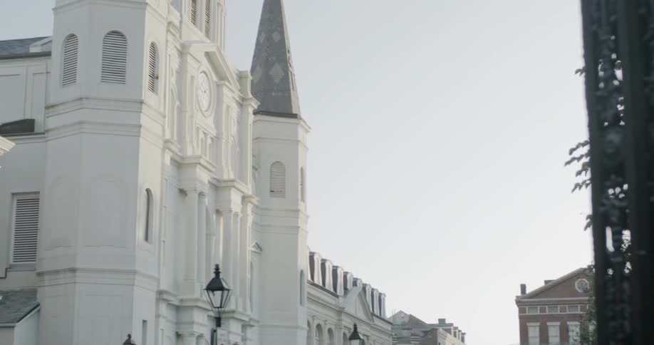 A white cathedral in a city with benches in front of it and brick buildings surrounding it