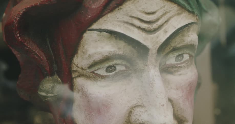 A painted and sculpted jester face with a furrowed brow