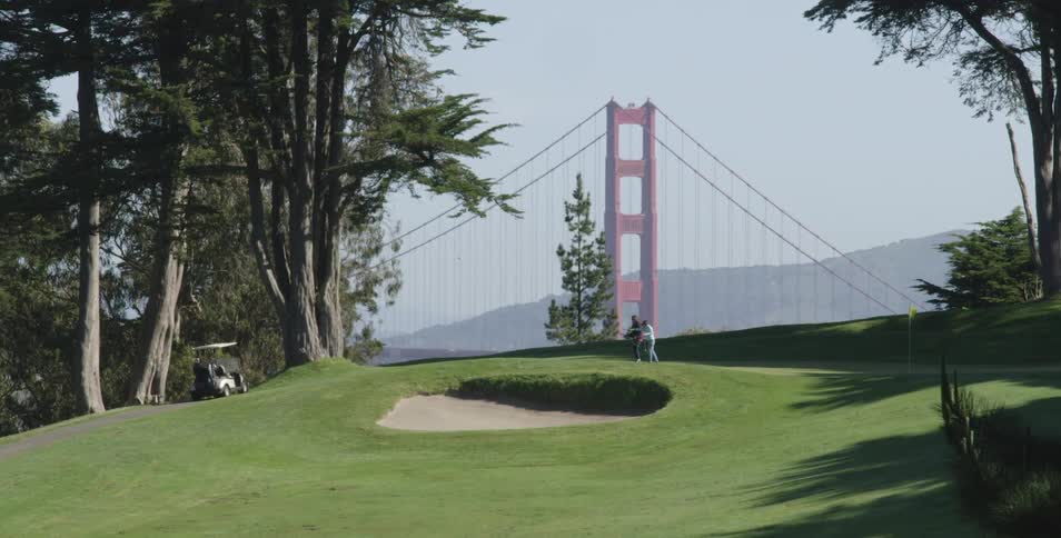 People stand on a golf course with the golden gate bridge behind them on a sunny day