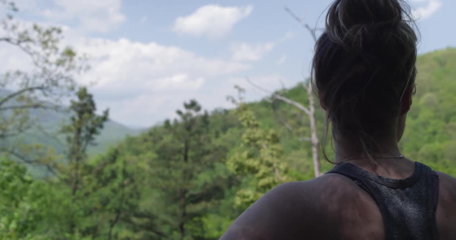 A young woman stands while looking around at the forest trees
