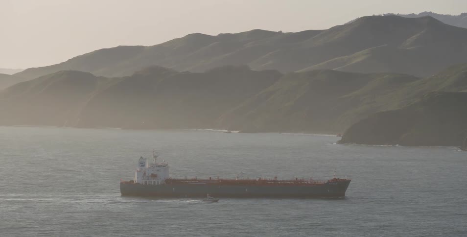 A ship floats just off the coast at sunset