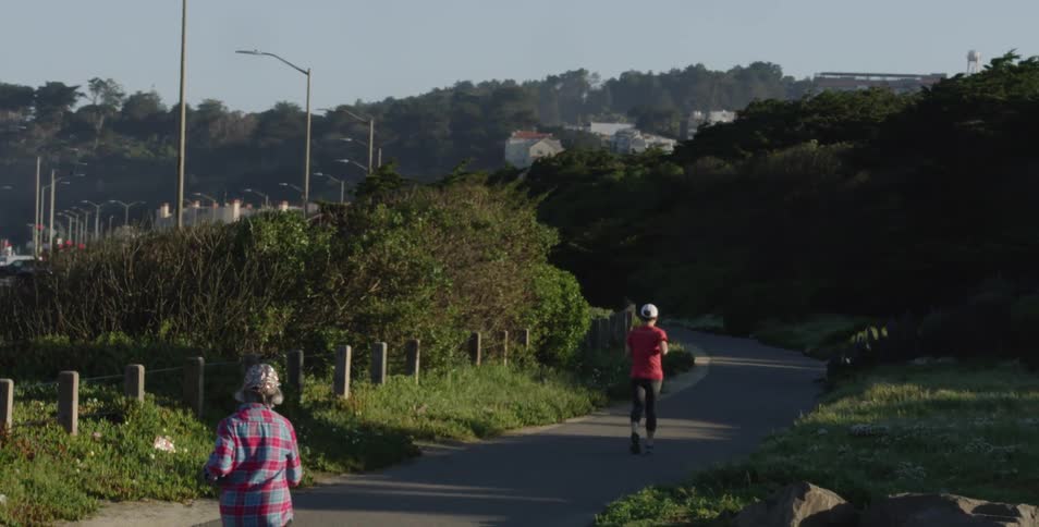 People jogging on a park path by a large car park