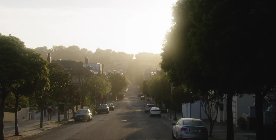 A suburban street with cars parked on both sides during a sunrise