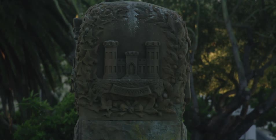 A stone statue with a building depicted on it surrounded by trees