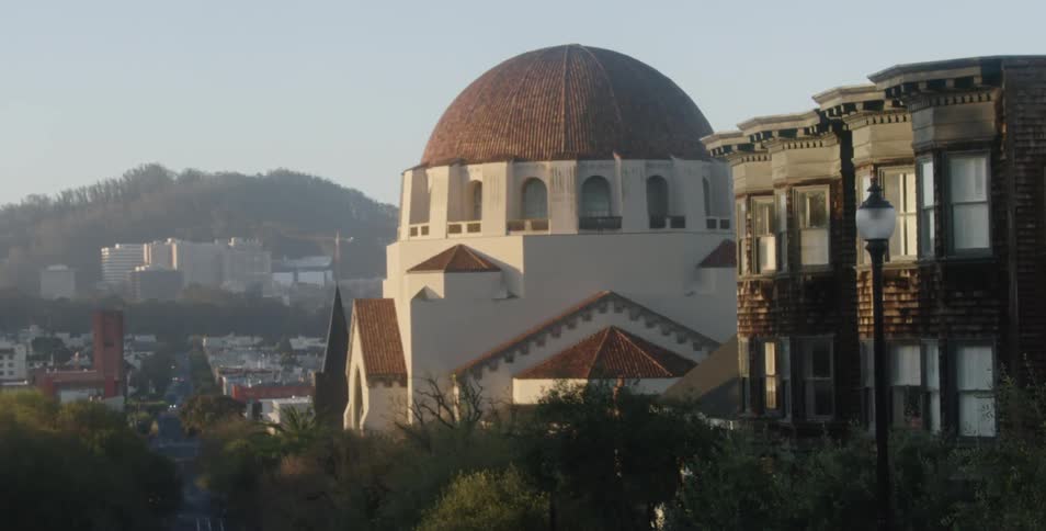 Amidst a city neighborhood a large temple with a rounded dome stands out from the adjacent buildings
