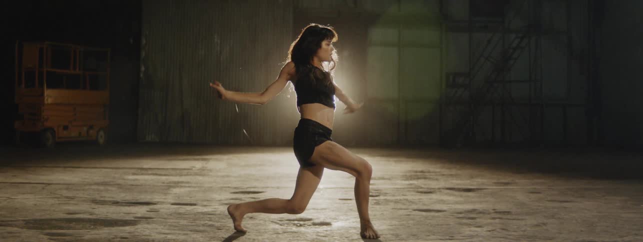 A woman dances in a spotlight in a dark room