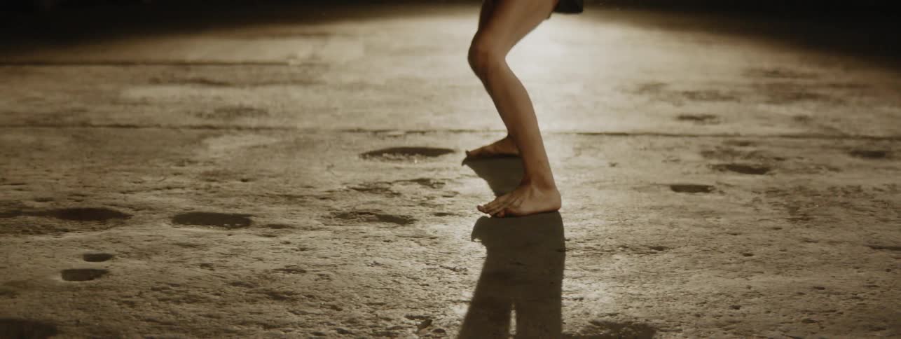 Dancer performing on a pocked surface with a bright light from one angle