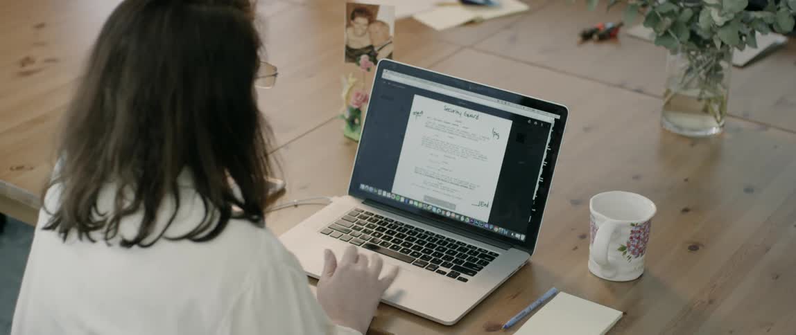 Woman wearing glasses uses laptop on table with pen and notebook by day