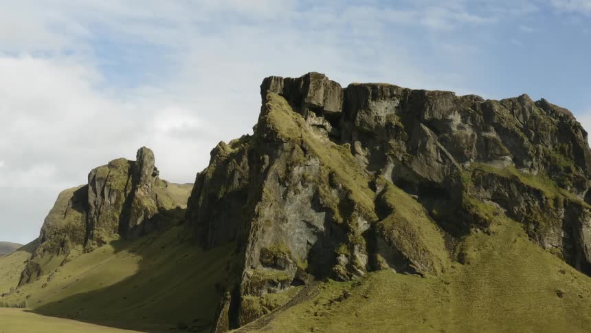 Mountains with green grass and moss rise to a sharp set of ridges in daylight