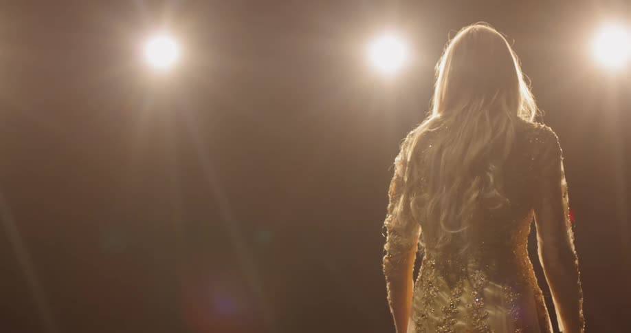 Bright spotlights shine on a woman in a gown