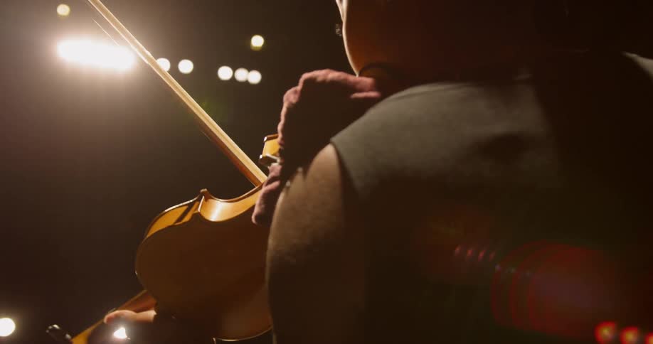 A woman plays violin under stage lights