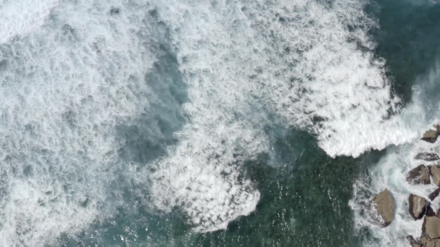 Waves and surf crash against rocky shore
