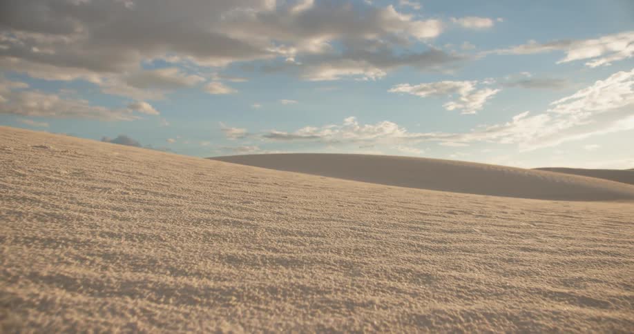 Wavy sand dunes under a partly cloudy sky