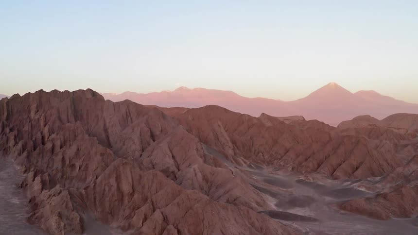 The camera flies over a desert with eroded mountains rising from it