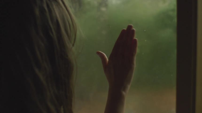 A woman wipes mist off of a window with her hand