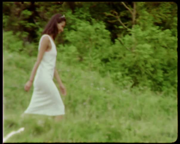 A woman in a white dress smiles while walking in a grassy field