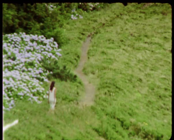 Woman wearing white dress walks on the forest path next to the flowers