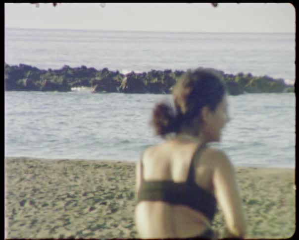 A woman is performing yoga poses atop a towel on the beach at the ocean shoreline