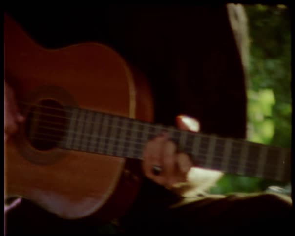 A man plays an acoustic guitar outside on a summer day