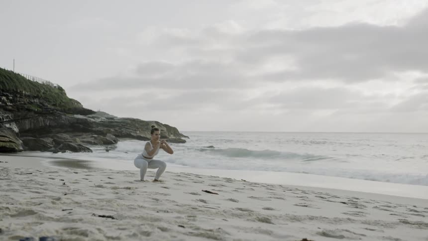 Woman does squats on the beach