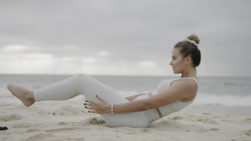 Woman in white leggings working out on the sand next to the ocean