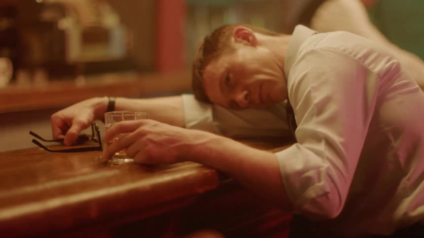 Man with his head on the bar counter holds drink glass and looks at it in pub