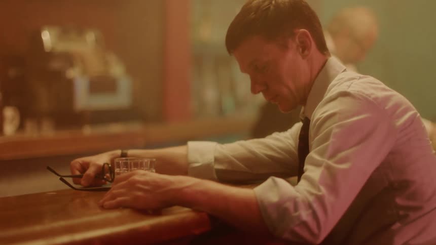 A man lifts his head up off of a bar counter as the bartender cleans up