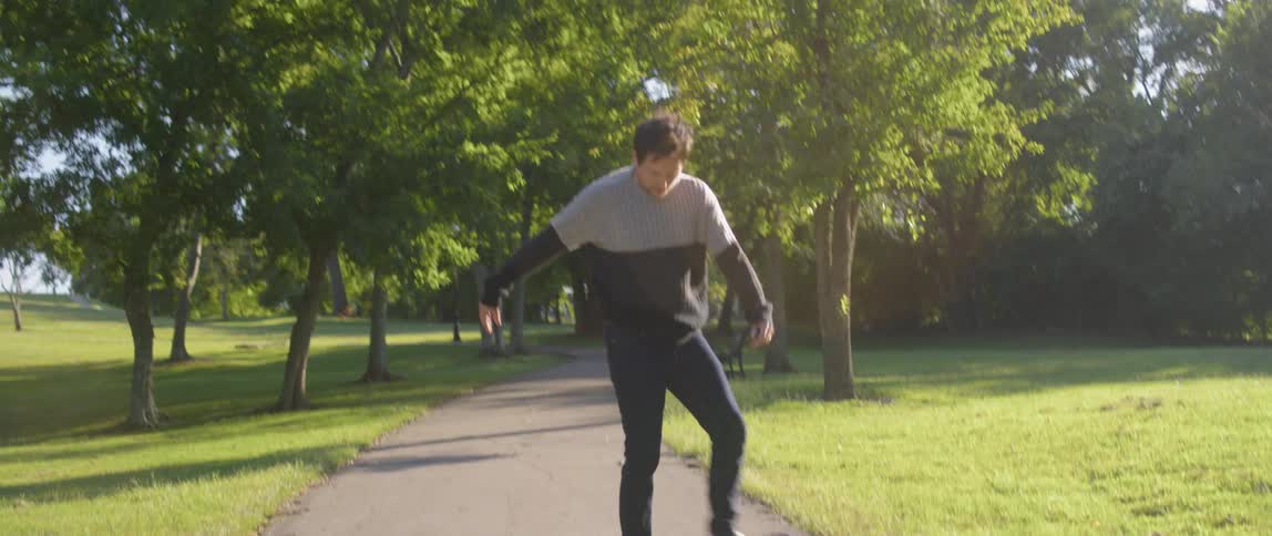 A man spinning on a skateboard on a walkway in a park