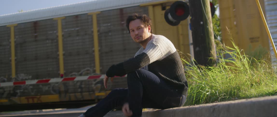 Man sitting next to a train tracks with a train going by