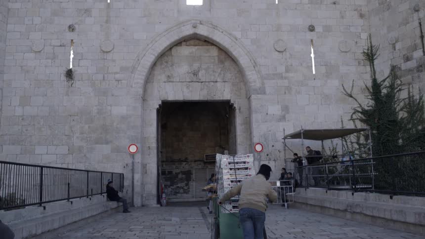 Man pushes stacked cart along paved walkway toward wide doorway in castle
