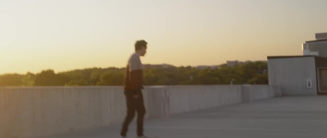 Young man skateboards on rooftop at sunset