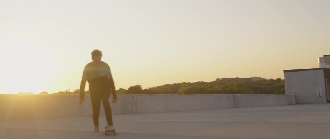 Man rides a skateboard on a rooftop at sunset