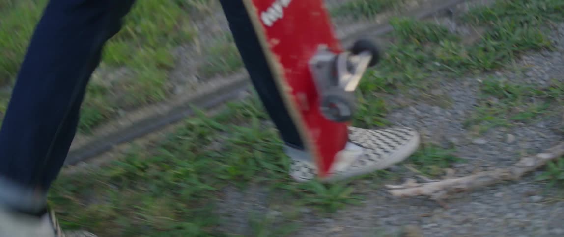 A man walking on the grass holding a skateboard