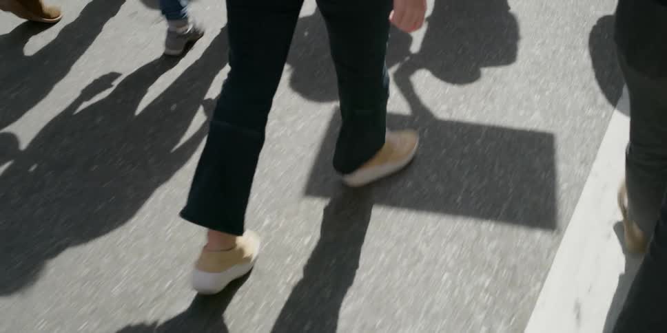 The legs feet and shadows of protesters walking down a street carrying signs