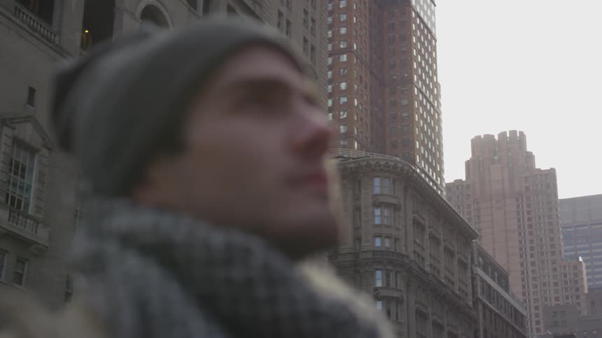 A man wrapped up warm stands in a city street of tall buildings