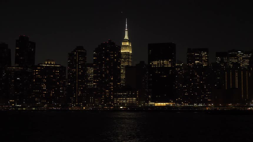 Cars and a boat move through a coastal city at night