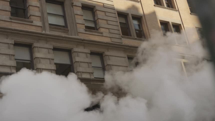Smoke rolls down a city street in front of a building