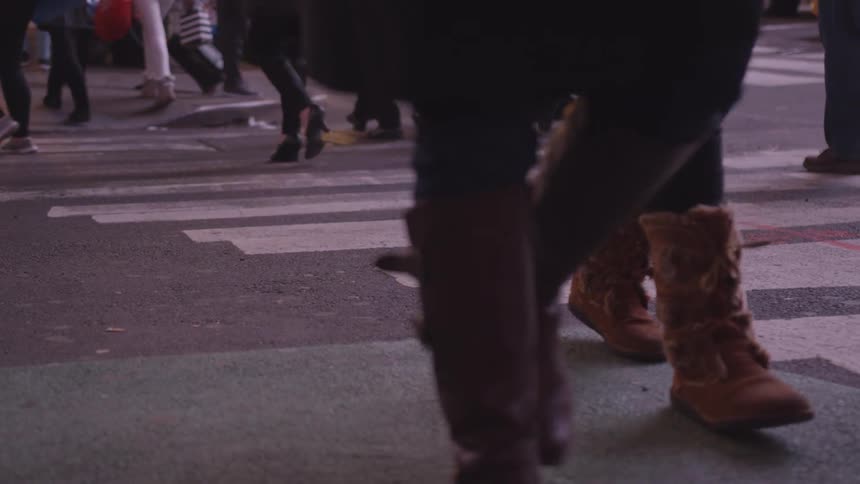 The legs and feet of people walking across a street wearing boots