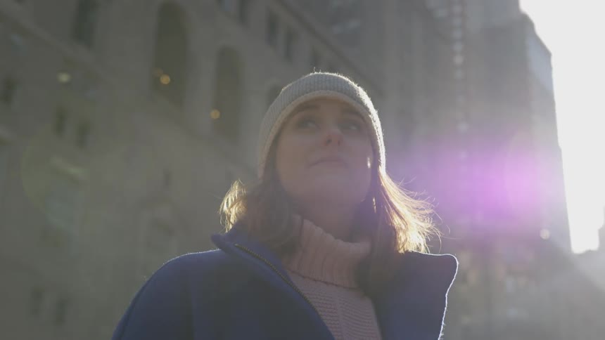 Woman wearing winter clothes stands and looks up at tall buildings