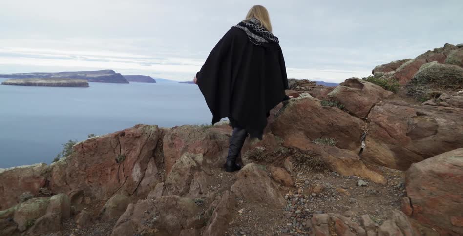 A woman climbing up a hill towards a coastline on a cloudy day