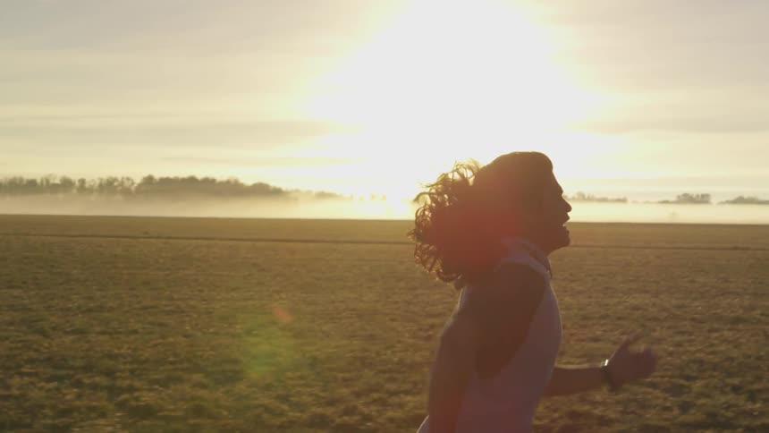A man with long hair runs on a field at sunset