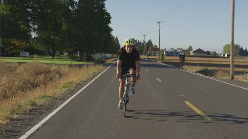 Man on bicycle rides towards camera on road