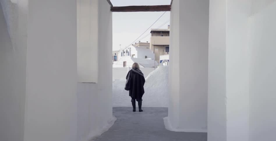 A woman stands between columns looking outwards towards the city