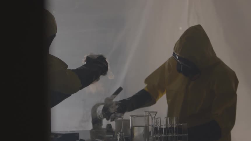Chemists in yellow hazmat suits pouring chemicals