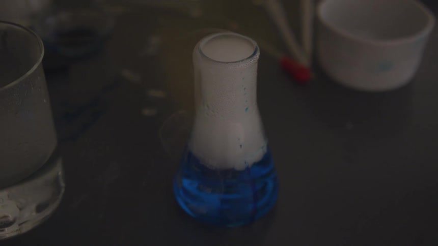 A blue solution bubbles and smokes in a beaker